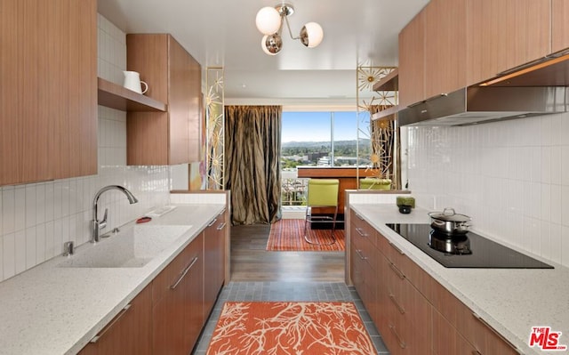 kitchen with black electric stovetop, light stone countertops, sink, and decorative backsplash