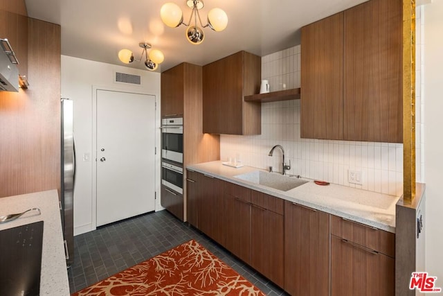 kitchen with sink, dark tile patterned floors, stainless steel appliances, light stone counters, and decorative backsplash