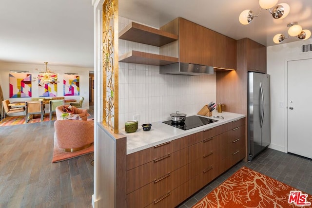 kitchen featuring dark wood-type flooring, stainless steel refrigerator, tasteful backsplash, black electric cooktop, and decorative light fixtures