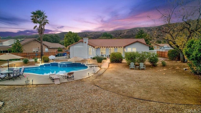 pool at dusk with an in ground hot tub and a patio