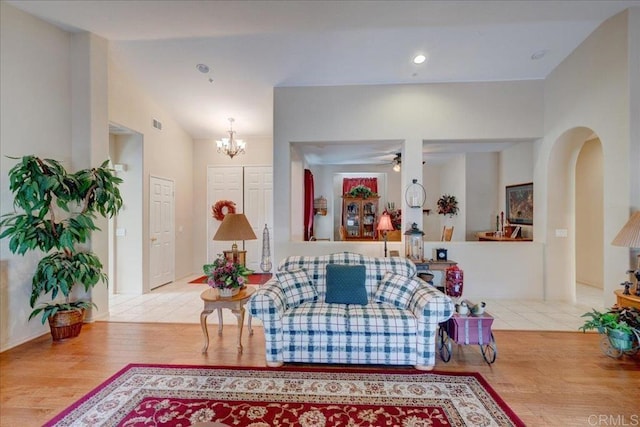 living room featuring lofted ceiling, ceiling fan with notable chandelier, and light hardwood / wood-style flooring