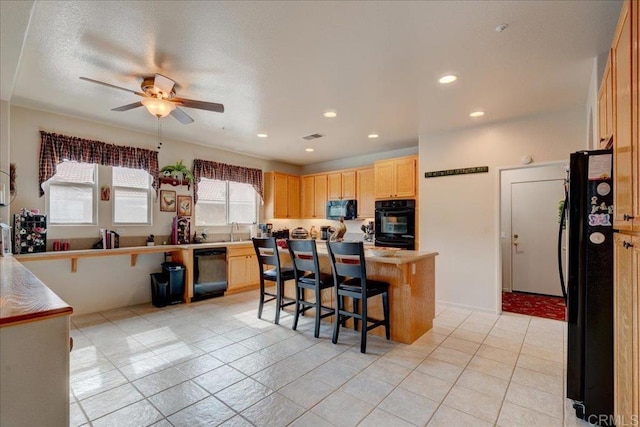 kitchen with light tile patterned floors, a breakfast bar area, ceiling fan, black appliances, and light brown cabinetry