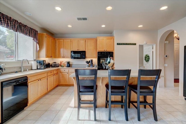 kitchen with light tile patterned flooring, a kitchen island, light brown cabinetry, a breakfast bar area, and black appliances