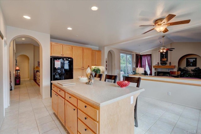 kitchen with lofted ceiling, a kitchen island, a kitchen breakfast bar, black fridge, and light brown cabinetry