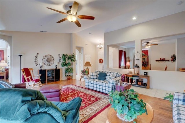 living room with ceiling fan with notable chandelier, light hardwood / wood-style floors, and vaulted ceiling