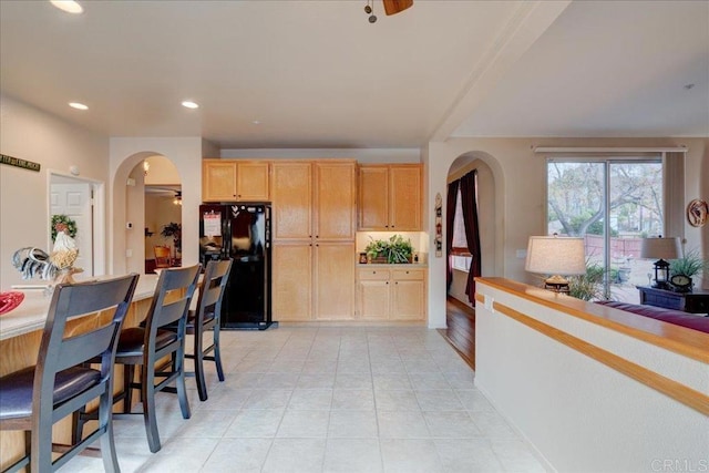 kitchen with light brown cabinetry, light tile patterned flooring, ceiling fan, and black fridge