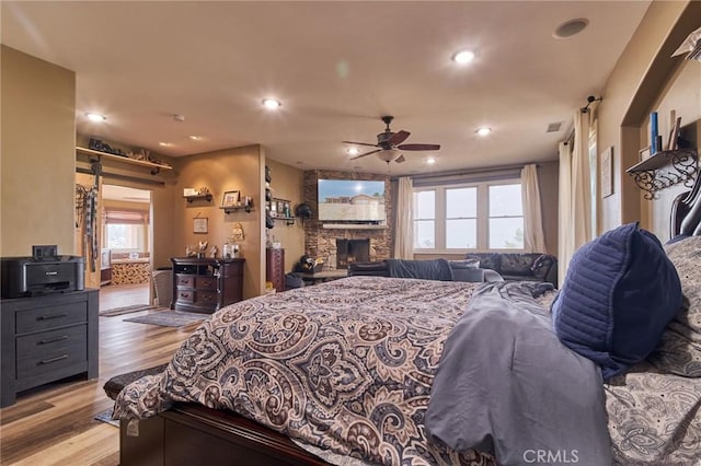 bedroom featuring multiple windows, a stone fireplace, and light wood-type flooring