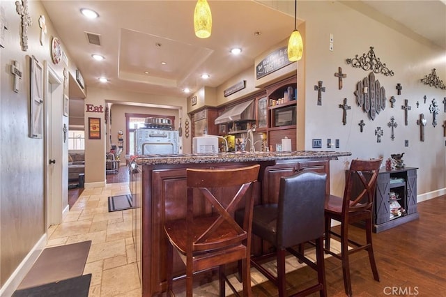 bar featuring a raised ceiling, black microwave, decorative light fixtures, and wall chimney exhaust hood