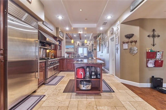 kitchen featuring a raised ceiling, dark stone countertops, wall chimney range hood, and premium appliances