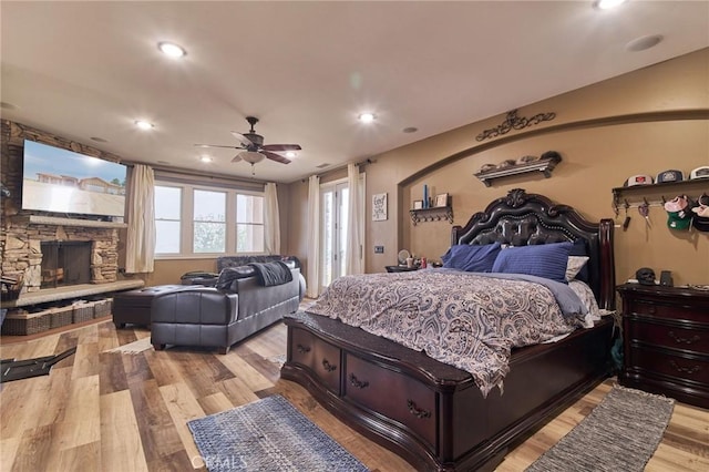 bedroom featuring ceiling fan, a stone fireplace, and light hardwood / wood-style floors