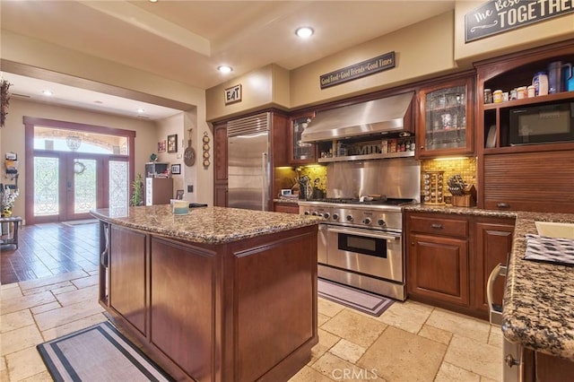 kitchen with backsplash, a kitchen island, range hood, premium appliances, and stone countertops