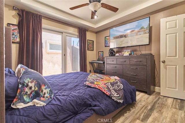 bedroom featuring ceiling fan, access to exterior, a raised ceiling, and light wood-type flooring