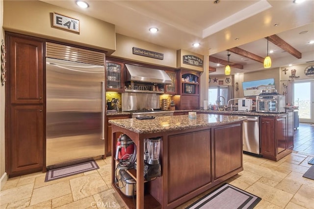 kitchen with dark stone countertops, appliances with stainless steel finishes, a center island, and wall chimney range hood