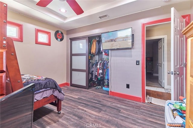 bedroom featuring ceiling fan, dark hardwood / wood-style flooring, a raised ceiling, and a closet