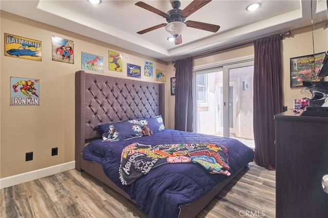 bedroom with hardwood / wood-style floors, access to outside, a raised ceiling, and ceiling fan