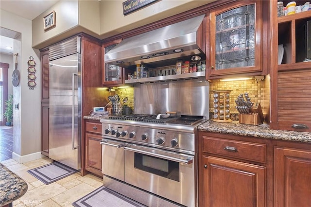 kitchen featuring high end appliances, range hood, light stone counters, and backsplash