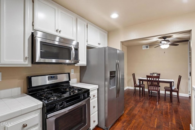 kitchen with appliances with stainless steel finishes, white cabinets, tile counters, ceiling fan, and dark wood-type flooring