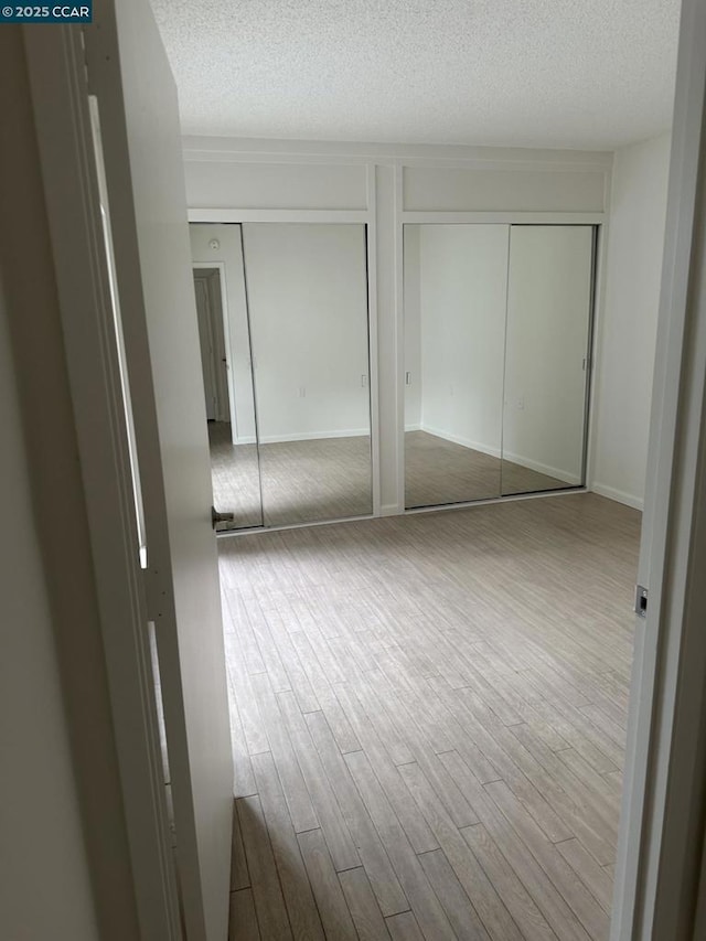 unfurnished bedroom featuring hardwood / wood-style flooring, a textured ceiling, and multiple closets