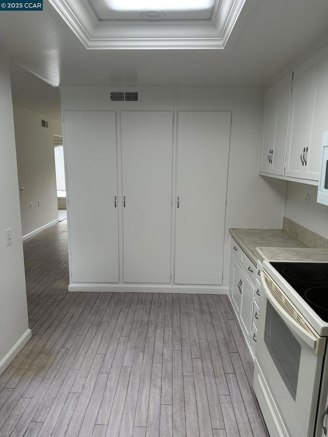 kitchen featuring white cabinetry, white appliances, light hardwood / wood-style floors, and a tray ceiling