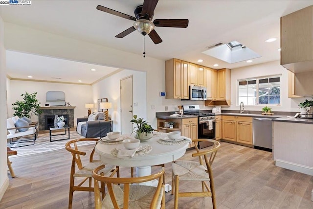 kitchen featuring sink, appliances with stainless steel finishes, a tiled fireplace, light brown cabinetry, and light wood-type flooring