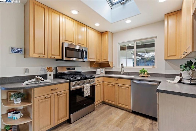 kitchen with appliances with stainless steel finishes, light brown cabinetry, a skylight, sink, and light wood-type flooring