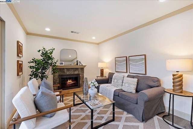 living room featuring crown molding, a tiled fireplace, and light wood-type flooring