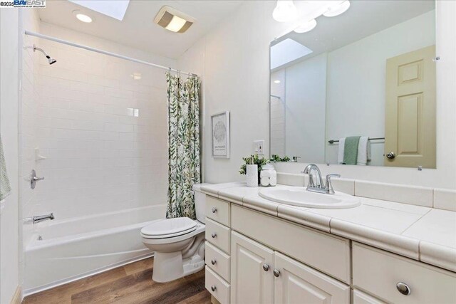 full bathroom featuring hardwood / wood-style flooring, shower / bath combo, vanity, and toilet