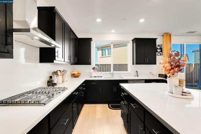 kitchen featuring sink, light hardwood / wood-style flooring, wall chimney exhaust hood, and appliances with stainless steel finishes