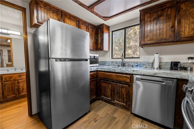 kitchen featuring stainless steel appliances, hardwood / wood-style flooring, sink, and light stone counters