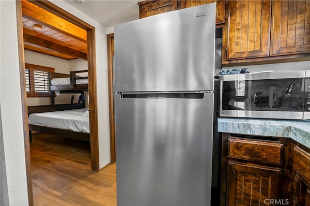 kitchen featuring stainless steel refrigerator, beamed ceiling, and light wood-type flooring