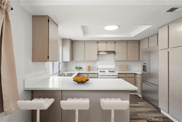 kitchen featuring sink, built in refrigerator, white range with gas cooktop, a raised ceiling, and kitchen peninsula