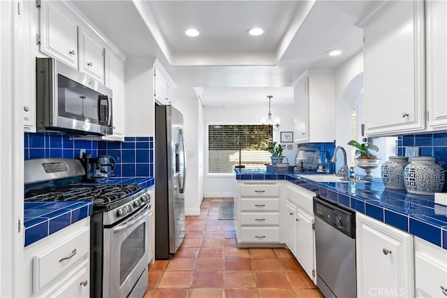 kitchen featuring sink, appliances with stainless steel finishes, tile counters, white cabinets, and a raised ceiling