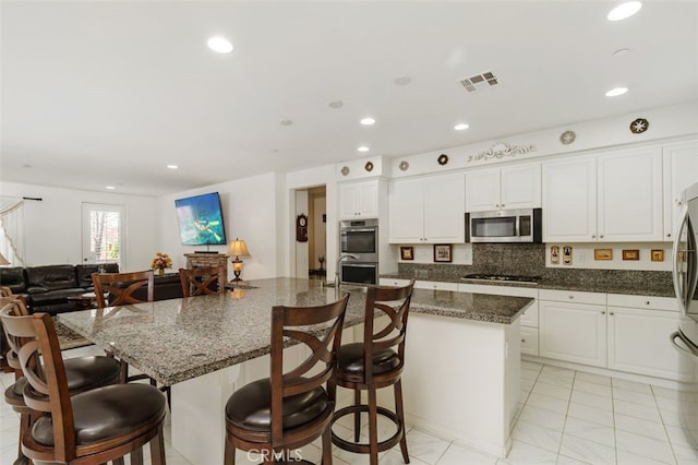 kitchen featuring appliances with stainless steel finishes, white cabinetry, a spacious island, tasteful backsplash, and dark stone counters