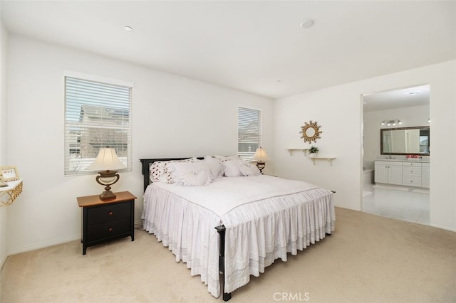 bedroom with multiple windows, light colored carpet, and ensuite bath