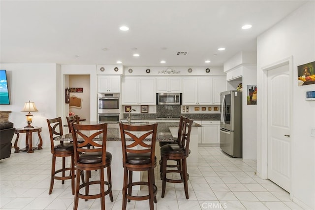 kitchen featuring a kitchen bar, sink, white cabinets, stainless steel appliances, and backsplash