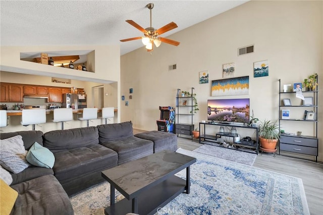 living room with ceiling fan, high vaulted ceiling, light hardwood / wood-style floors, and a textured ceiling