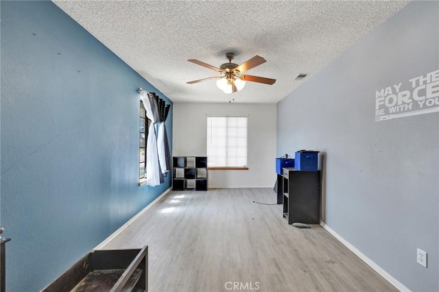 interior space with a textured ceiling, ceiling fan, and light hardwood / wood-style flooring