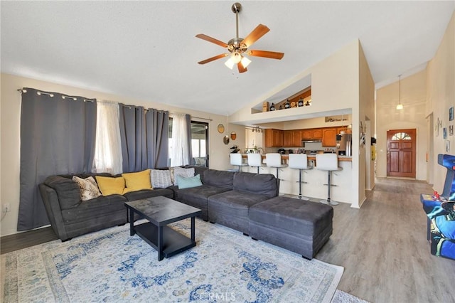 living room featuring ceiling fan, high vaulted ceiling, and light hardwood / wood-style flooring