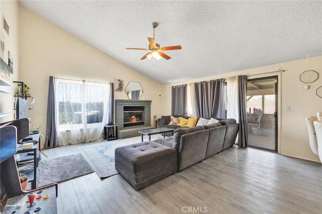 living room with ceiling fan, hardwood / wood-style floors, high vaulted ceiling, a textured ceiling, and a brick fireplace