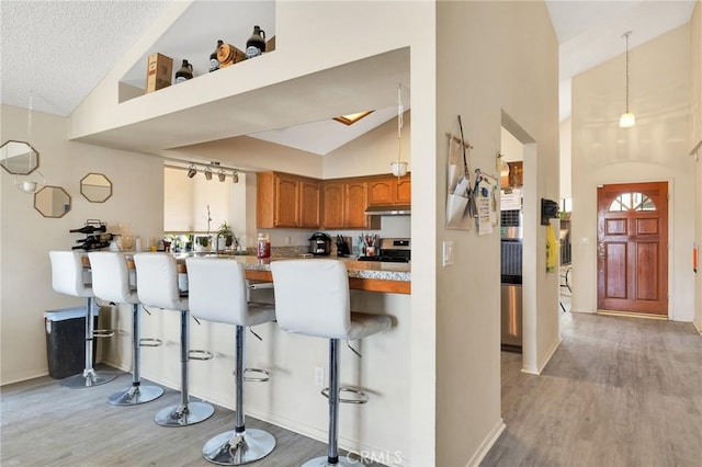 kitchen with a kitchen bar, stainless steel range with electric cooktop, hanging light fixtures, light hardwood / wood-style flooring, and kitchen peninsula