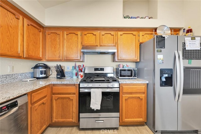 kitchen featuring vaulted ceiling, light stone countertops, light hardwood / wood-style floors, and appliances with stainless steel finishes