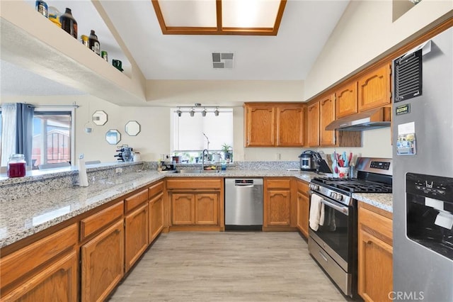 kitchen featuring lofted ceiling, sink, stainless steel appliances, light stone countertops, and light wood-type flooring