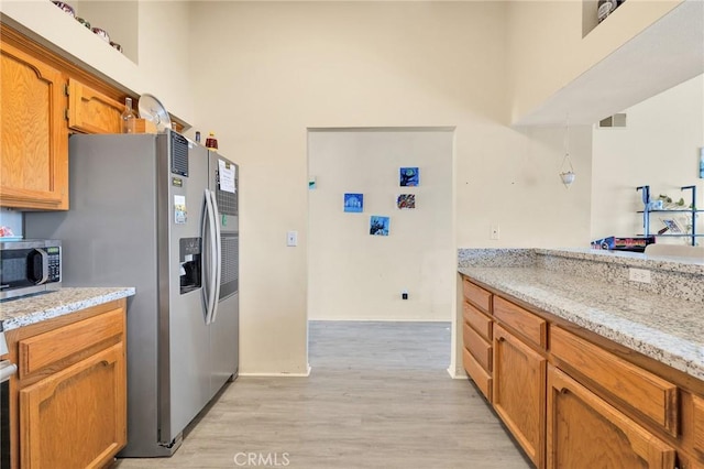 kitchen featuring light stone counters, a towering ceiling, light hardwood / wood-style floors, and appliances with stainless steel finishes