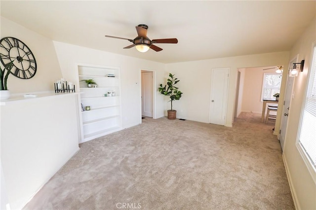 carpeted empty room featuring ceiling fan, plenty of natural light, and built in features