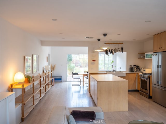 kitchen featuring a kitchen island, light brown cabinetry, premium appliances, hanging light fixtures, and light hardwood / wood-style floors