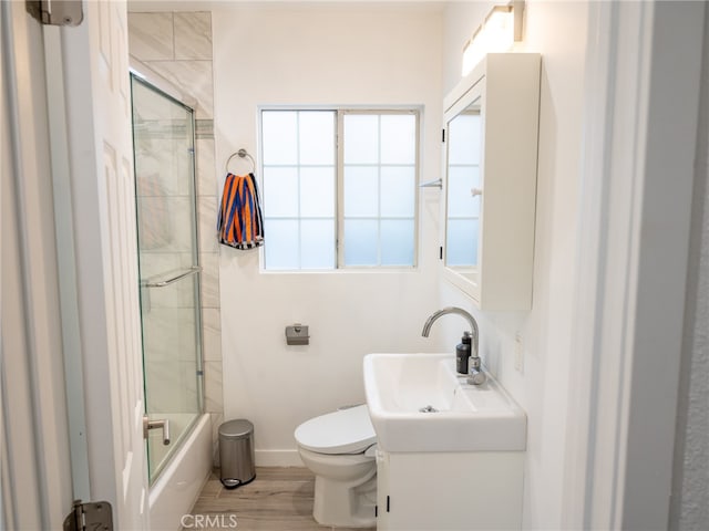 full bathroom featuring vanity, hardwood / wood-style flooring, bath / shower combo with glass door, and toilet