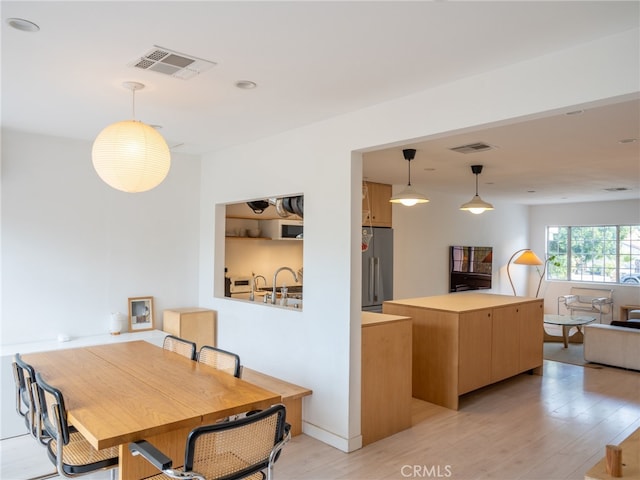 kitchen featuring light hardwood / wood-style flooring, hanging light fixtures, a center island, high quality fridge, and light brown cabinetry