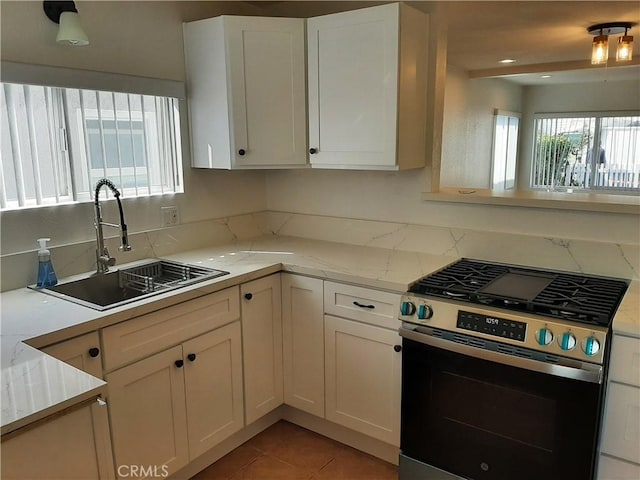 kitchen featuring light tile patterned floors, light stone counters, a sink, white cabinets, and stainless steel range with gas stovetop