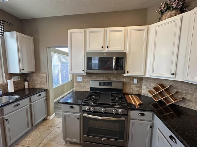 kitchen featuring appliances with stainless steel finishes, backsplash, white cabinets, light tile patterned flooring, and dark stone counters