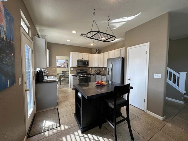 kitchen with a center island, light tile patterned floors, appliances with stainless steel finishes, decorative backsplash, and white cabinets